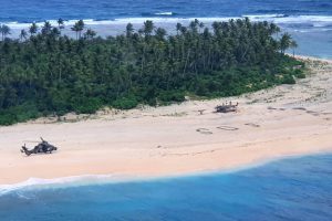 This handout photo taken on August 2, 2020 and received on August 4 from the Australian Defence Force shows an Australian Army ARH Tiger helicopter landing near the letters "SOS" (C) on a beach on Pikelot Island where three men were found in good condition after being missing for three days. - Three Micronesian sailors stranded on a tiny island in the remote Western Pacific were rescued after Australian and US warplanes spotted a giant "SOS" they had scrawled on the beach, officials said. (Photo by Handout / Australian Defence Force / AFP) / RESTRICTED TO EDITORIAL USE - MANDATORY CREDIT "AFP PHOTO / AUSTRALIAN DEFENCE FORCE" - NO MARKETING - NO ADVERTISING CAMPAIGNS - DISTRIBUTED AS A SERVICE TO CLIENTS